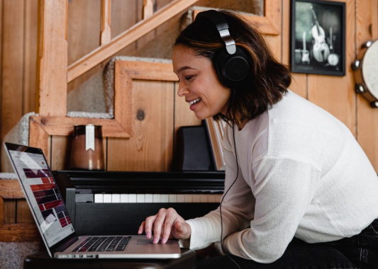 Woman with headphones on sitting at computer smiling and seeming content.