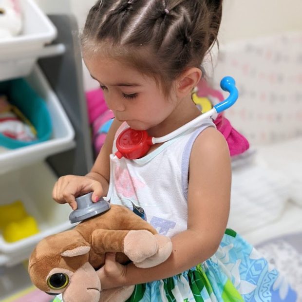 Toddler girl using a play stethoscope to check on her stuffed animal
