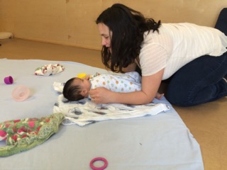 Young baby laying on their back on sheeted rug with mom leaning close to them at RIE® Parent Infant Guidance Class™