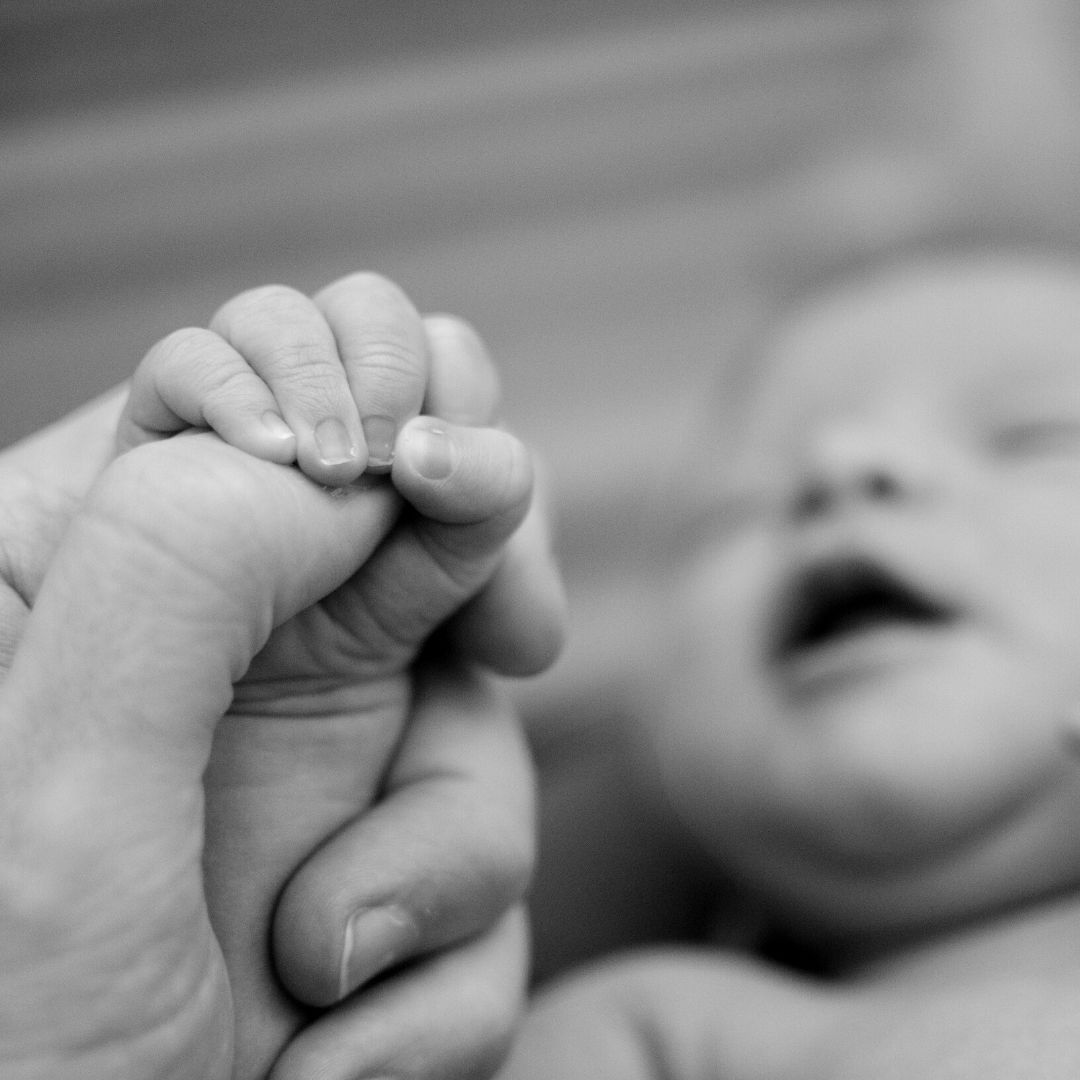 Newborn holding onto adult's thumb while peacefully sleeping